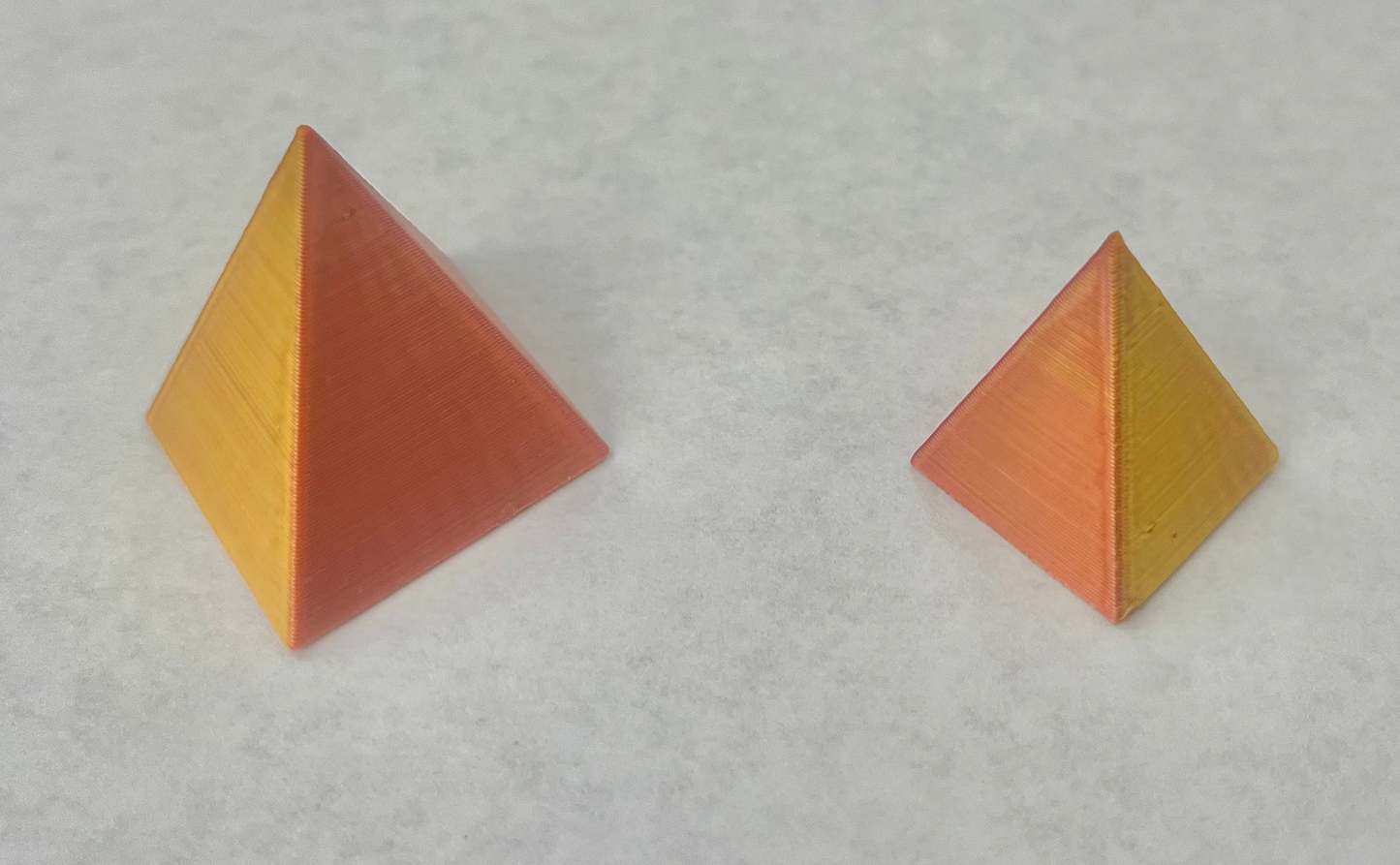 Two dual pyramids with gold and orange colors on a white surface.