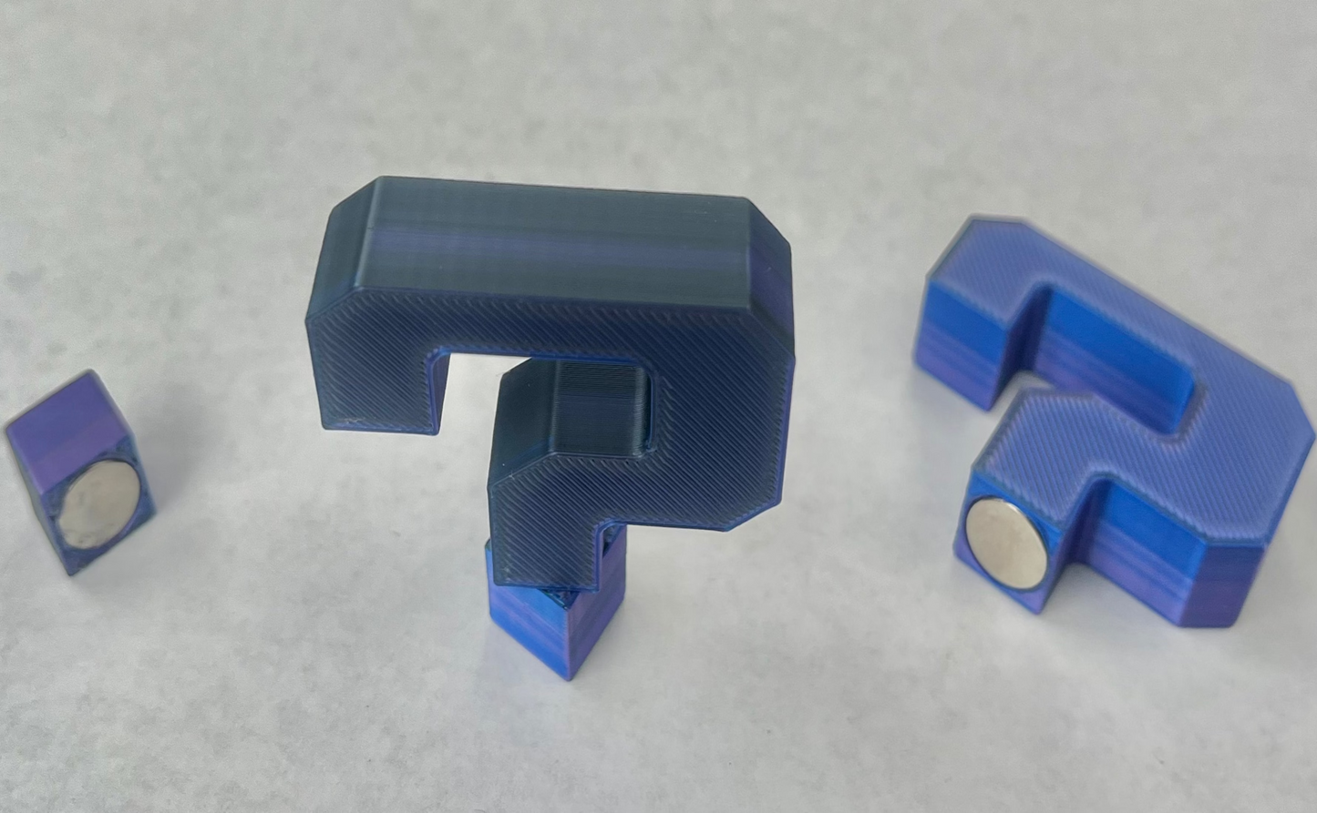 A collection of blue magnetic hat brim accessories in various shapes, including a question mark, a small square, and a larger rectangular piece.