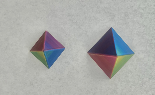 Two geometric construction toys with blue, green, purple, and metallic colors, shaped like dual pyramids.